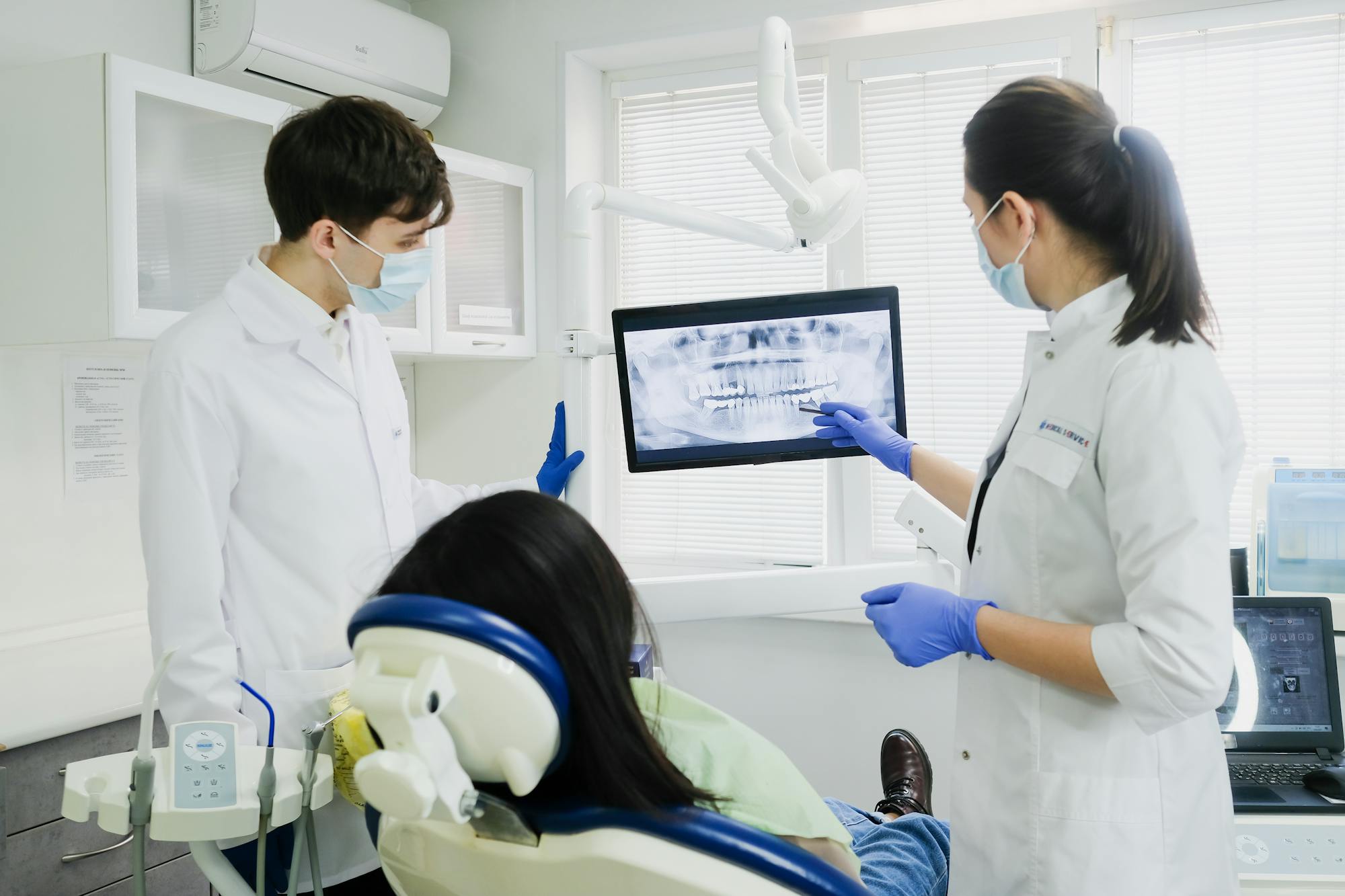 Dental professionals reviewing a panoramic X‑ray with a seated patient in a modern clinic.